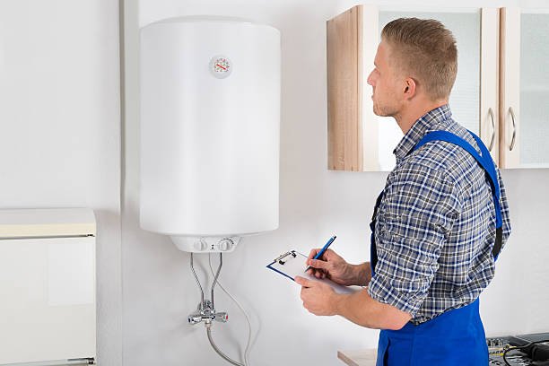 young man writing on clipboard while looking at electric boiler